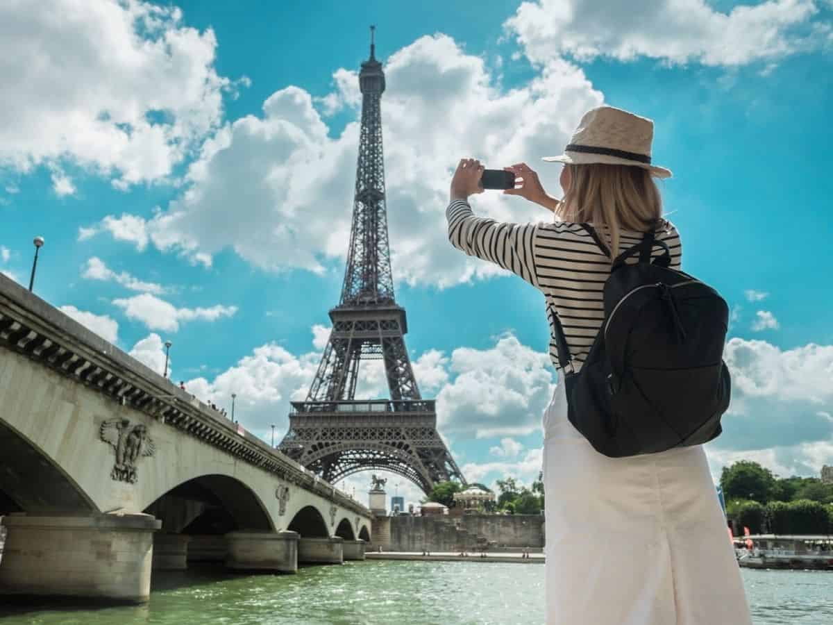 Woman wearing a backpack taking a photo of the Eiffel Tower