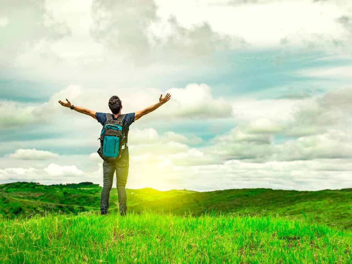 A man is standing on a green field with his arms outstretched.