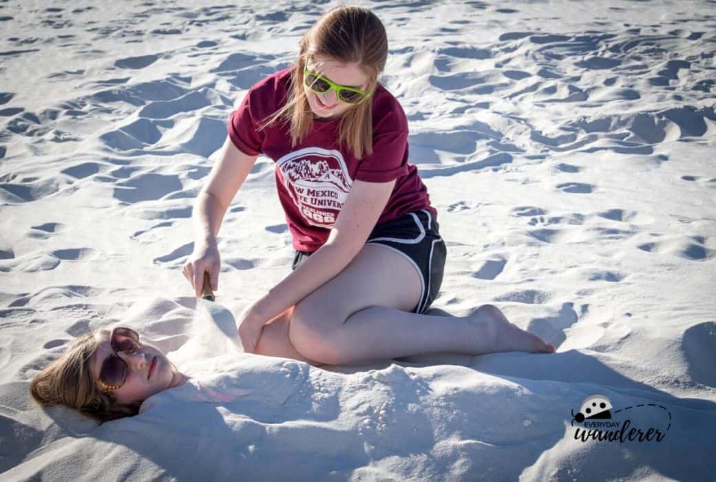 A girl buries another in the sandy white dunes at White Sands New Mexico