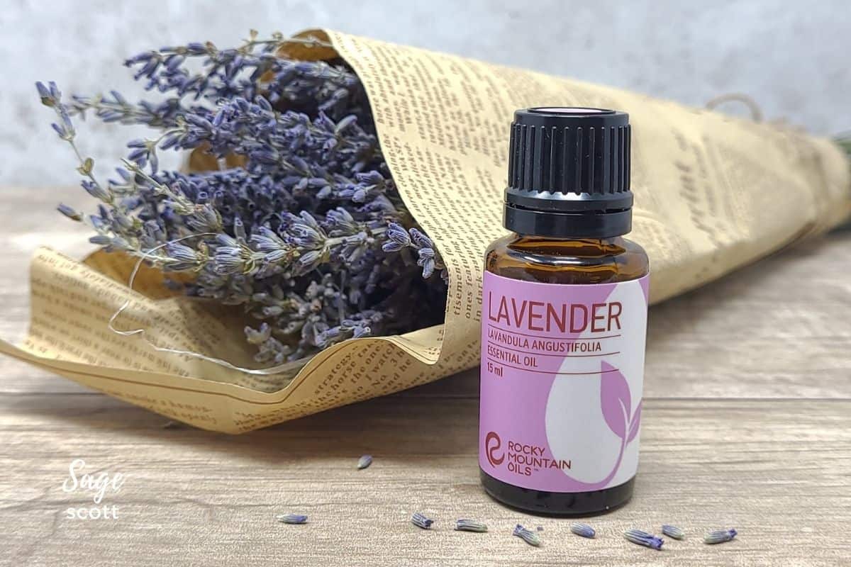 A bottle of lavender essential oil on a wood table with a dried lavender bouquet