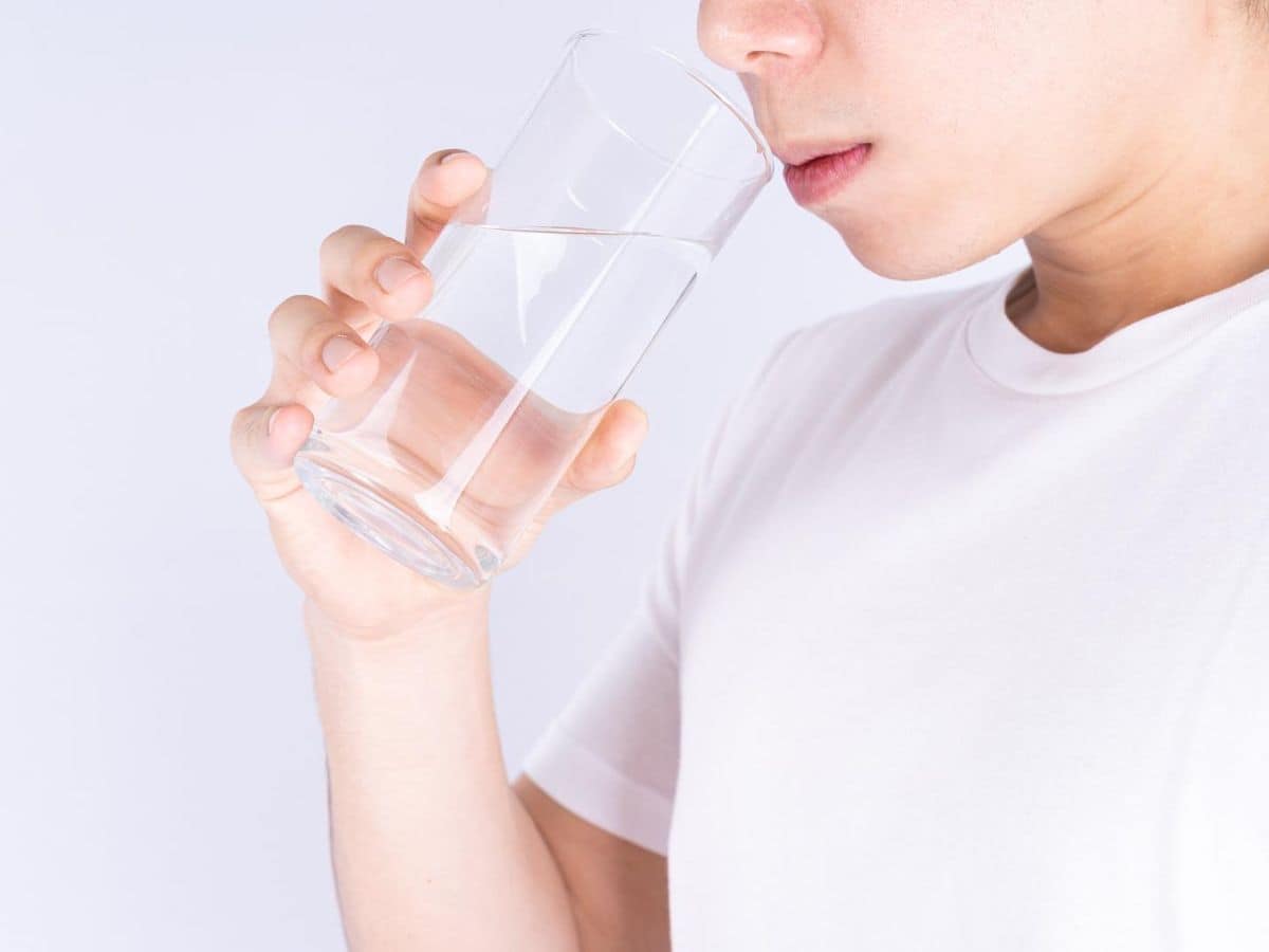 A woman drinking water from a glass on a white background.