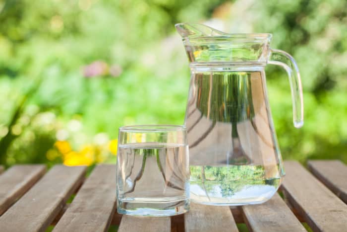 Pitcher and glass of water on a wooden table outdoors