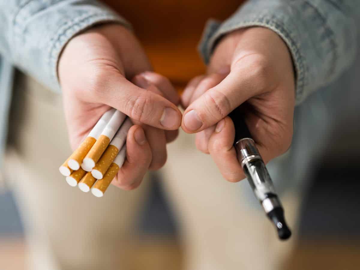 A man with a handful of cigarettes and an e-cigarette in his hands
