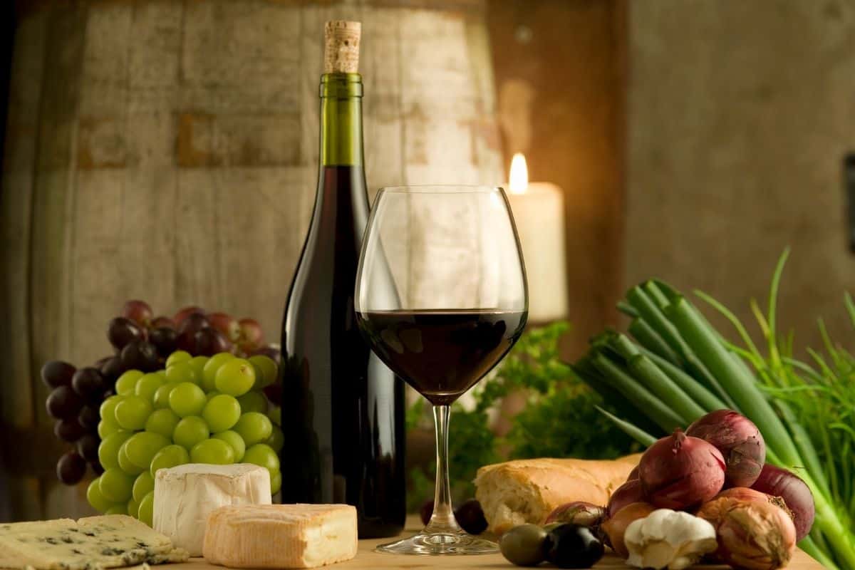 A glass of red wine next to grapes, cheese, and other ingredients