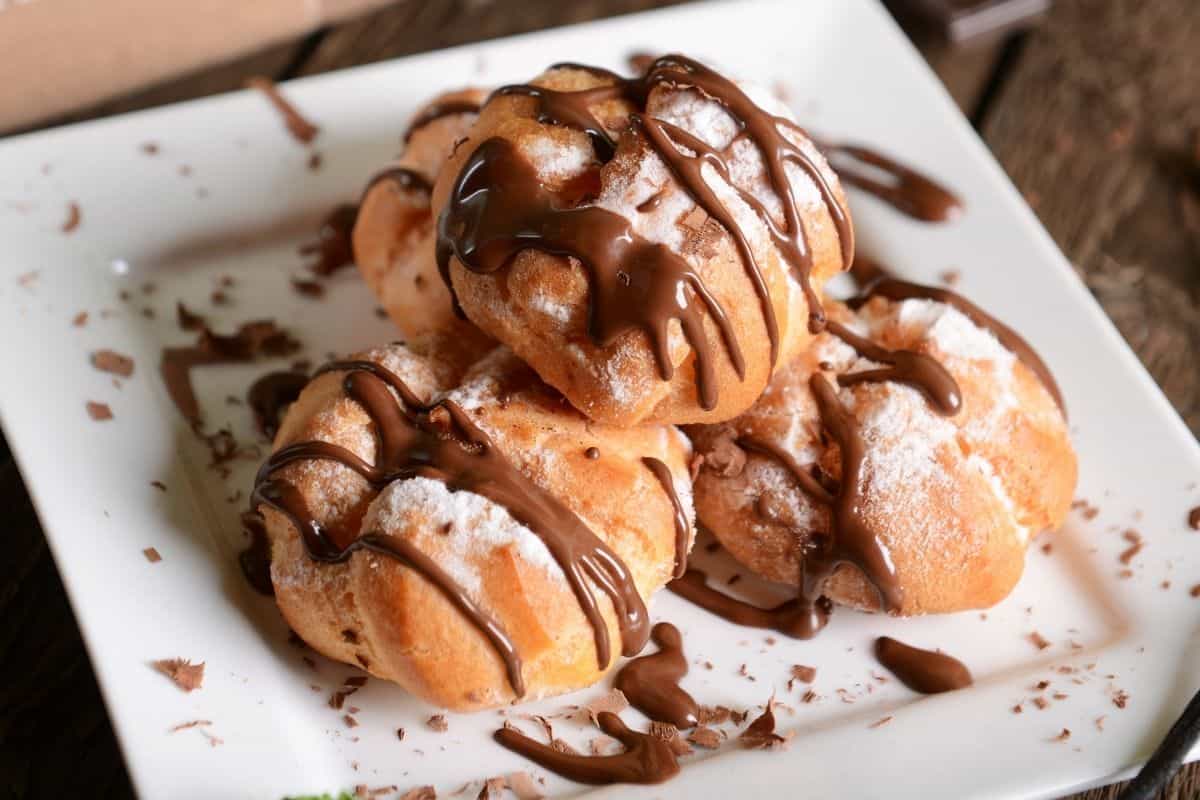 A plate stacked with chocolate-drizzled profiteroles