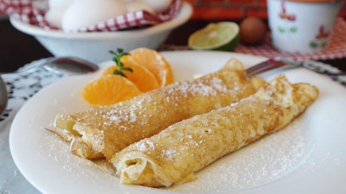 A plate of powder sugar dusted sweet crepes