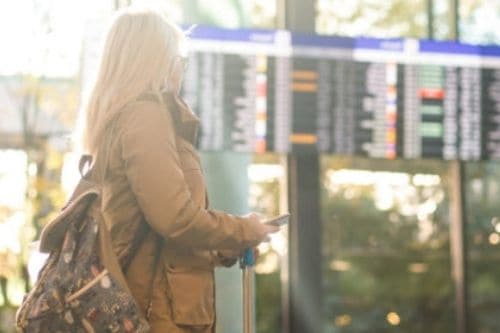 blonde woman looking at travel board in airport