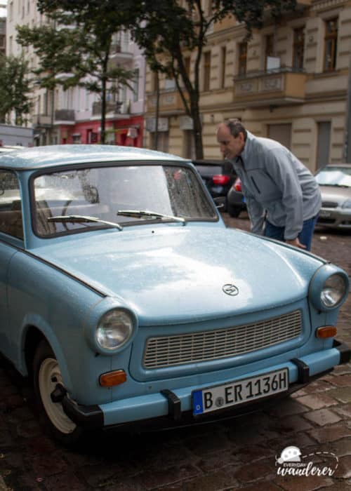 A tall man looking in a light blue Trabant car.