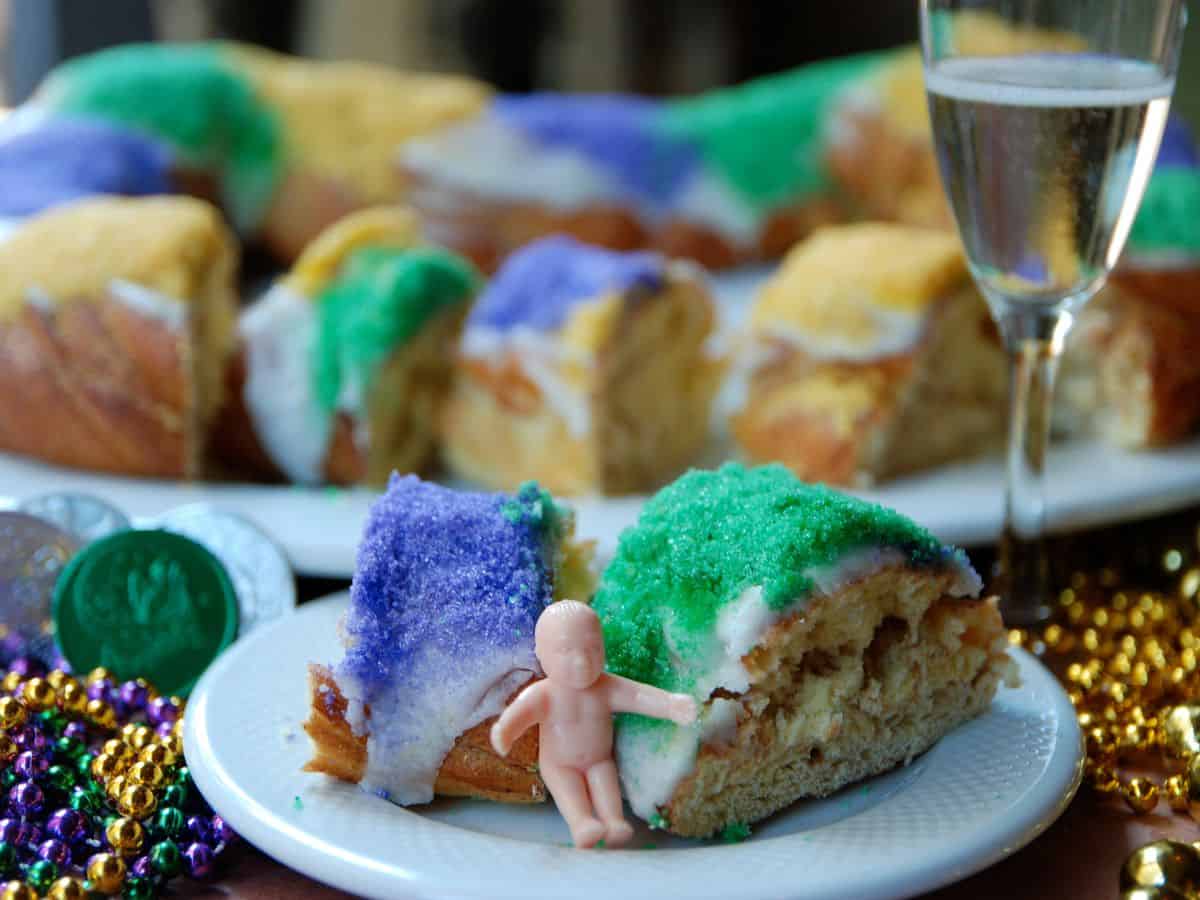 A plate of king cake on a table decorated for Mardi Gras cake next to a glass of champagne.