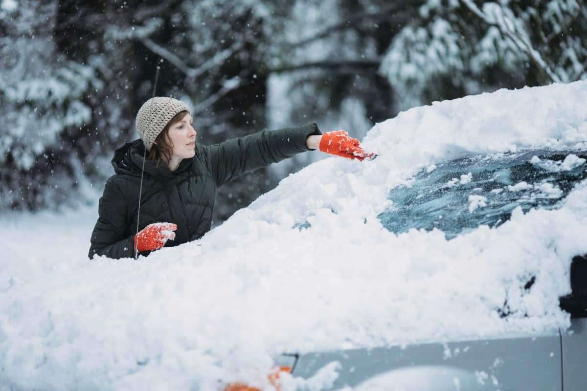A woman scraping snow and ice off a car's windshield