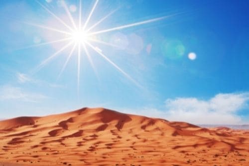 The sun shining above a sand dune in the desert