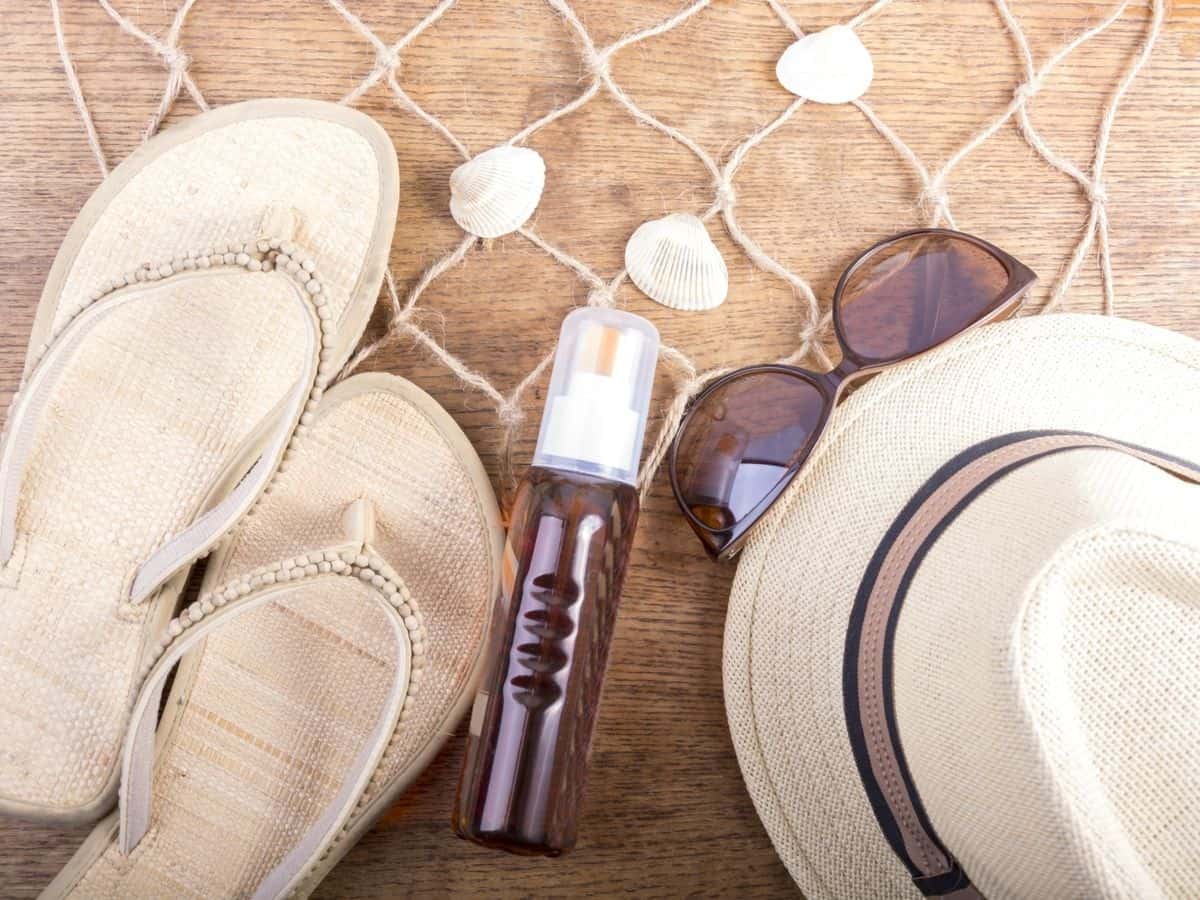 Bottle of essential oil with sandals, sunglasses, and a hat