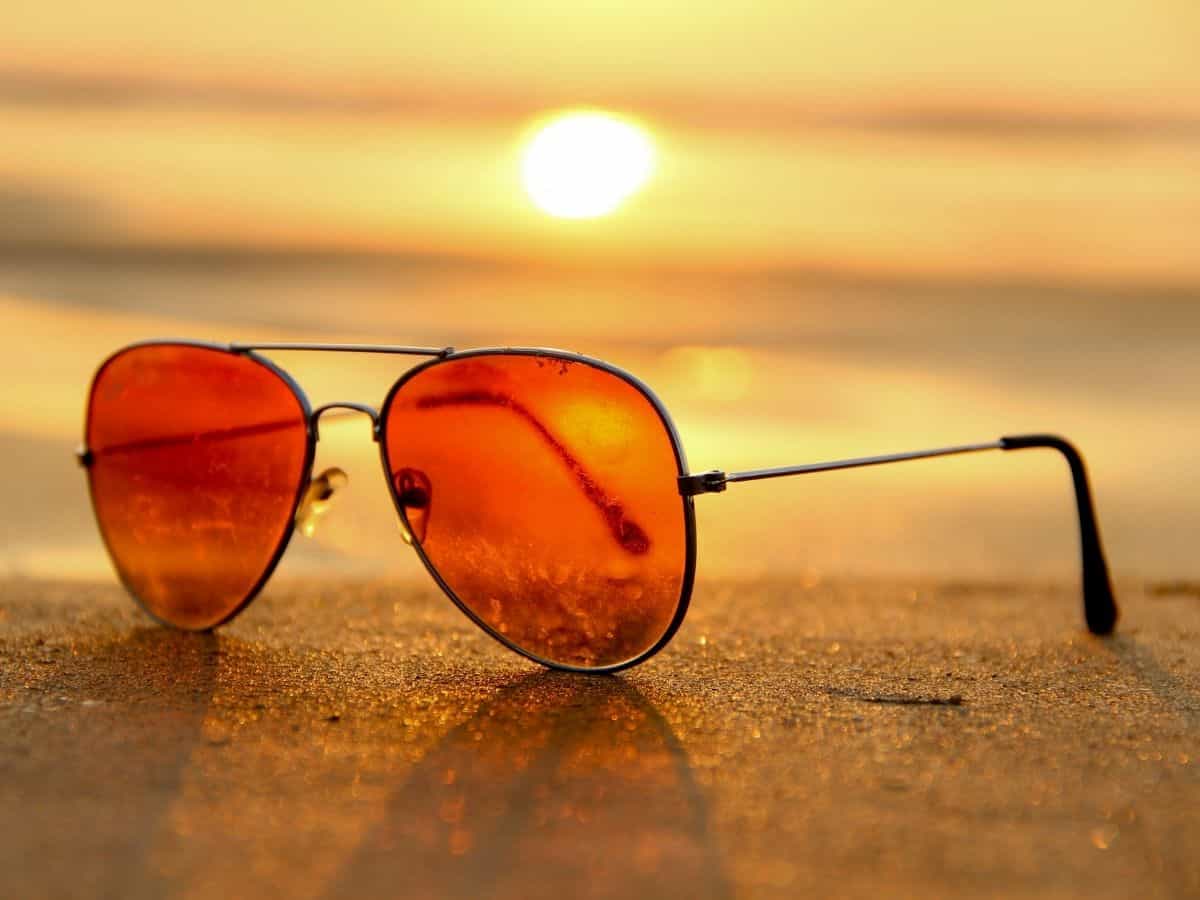 A pair of rose-colored sunglasses on the sand as the sun starts to set