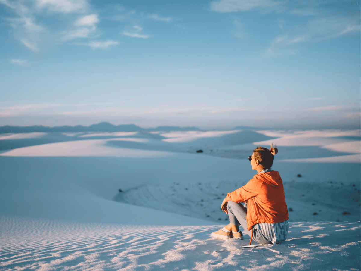 Woman in orange sweatshirt sitting in white sand