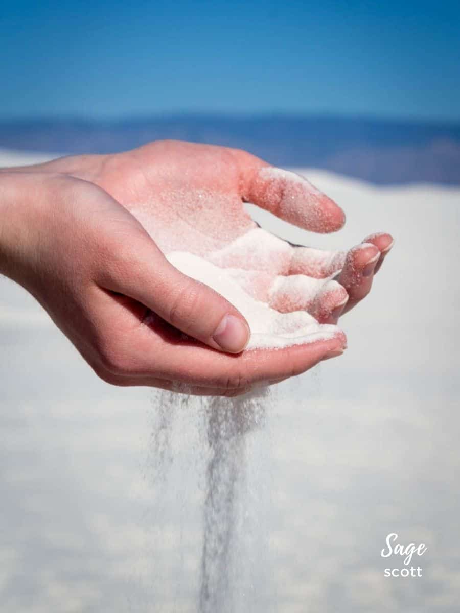 Soft white sand spilling through a young woman's hands