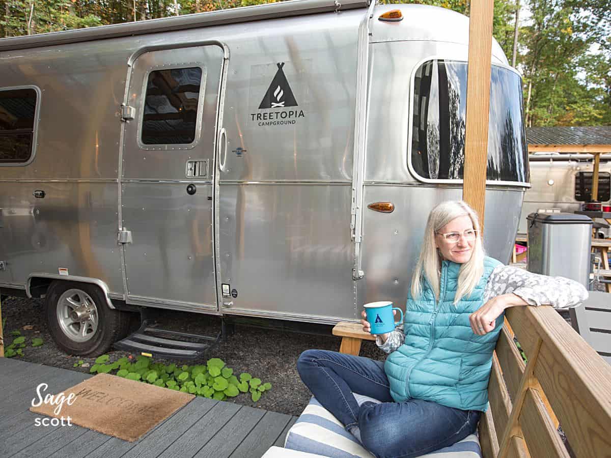Sage sipping coffee on the deck of a Treetopia Airstream hotel