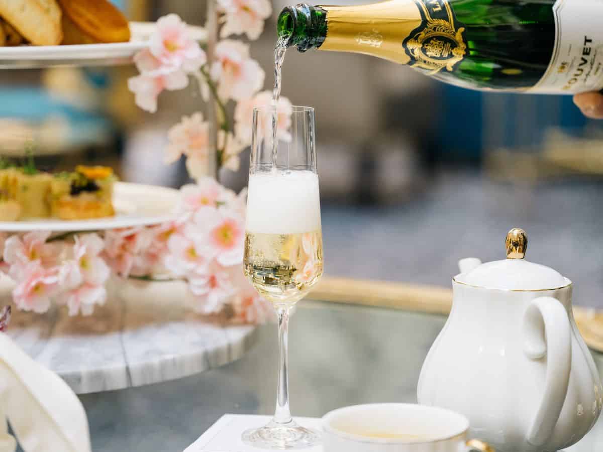 A person pouring champagne into a glass on a table during cherry blossom tea at the Waldorf Astoria in Washington DC.