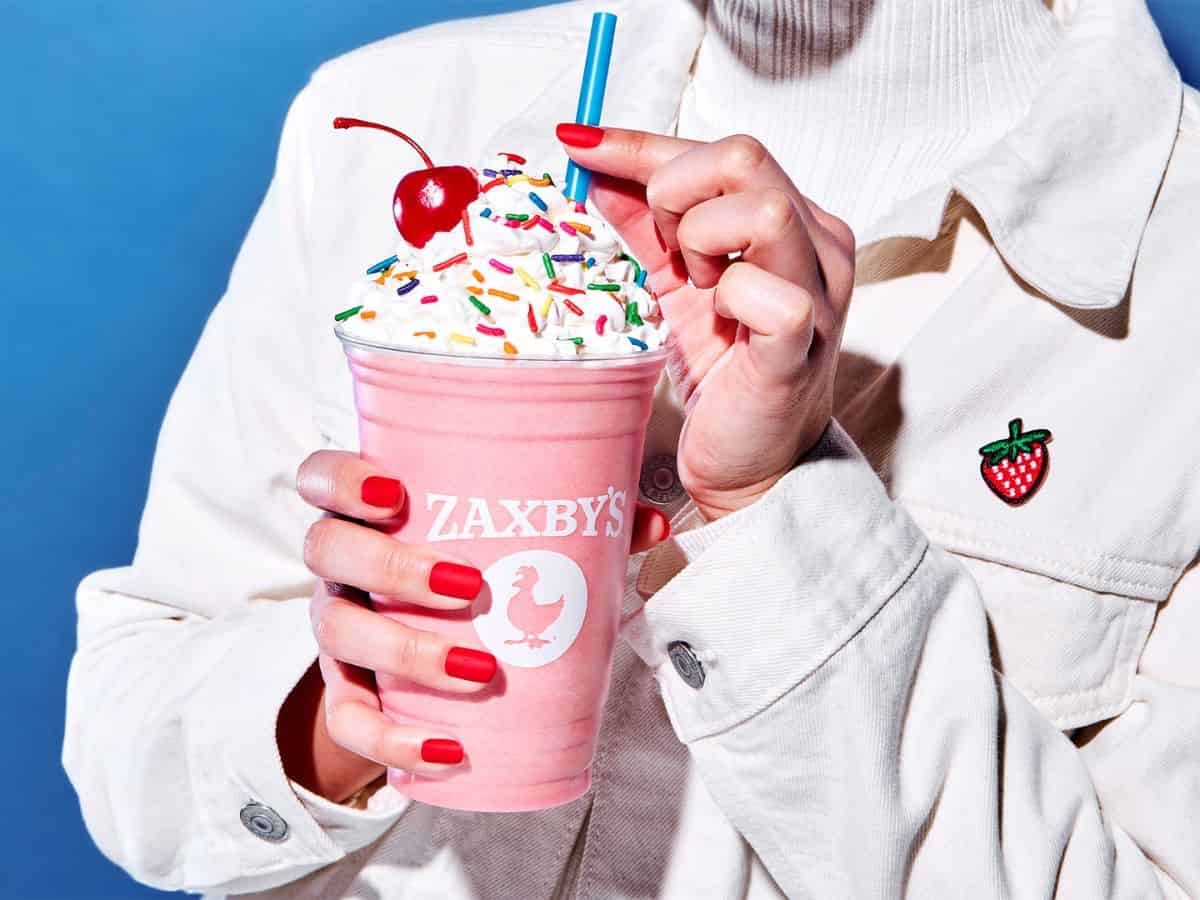 A woman holding a strawberry milkshake with sprinkles on it.