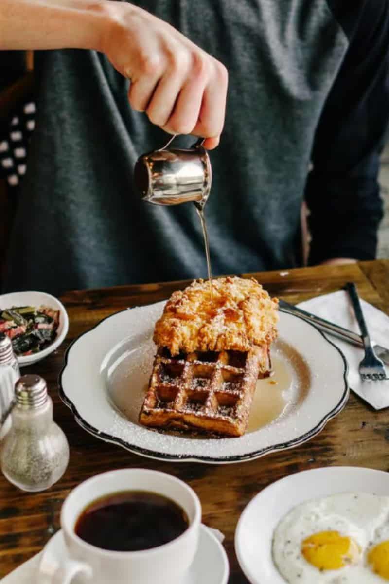 Man pouring maple syrup over a fried chicken topped pressed waffle at The Sassy Biscuit in Billings MT