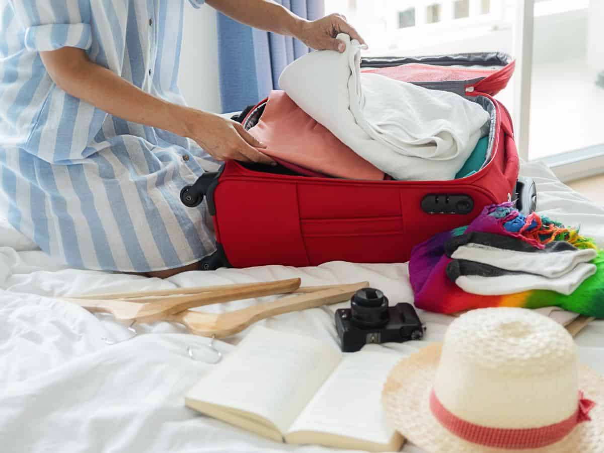 Woman in a blue and white striped shirt packing a red suitcase for a trip