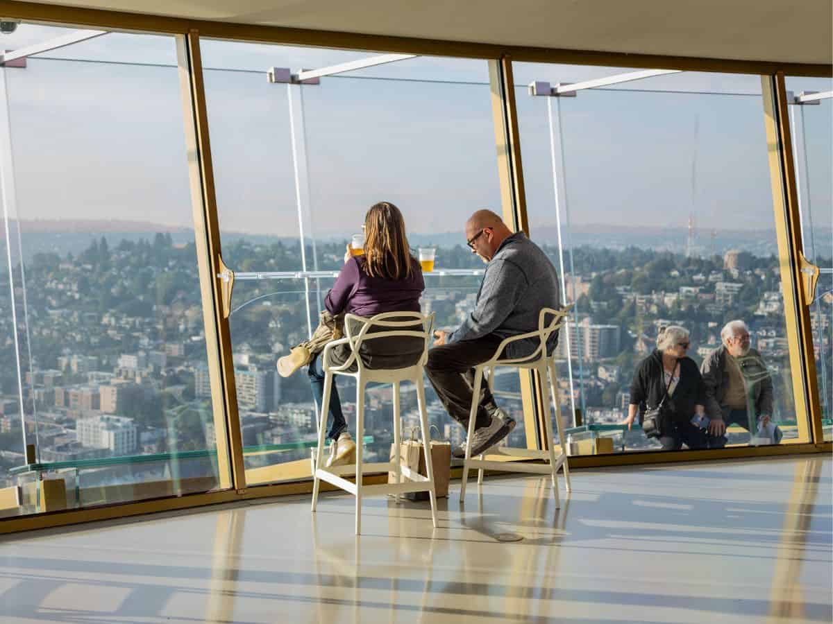 Two individuals sitting on chairs enjoying the view of a city while visiting the Space Needle.