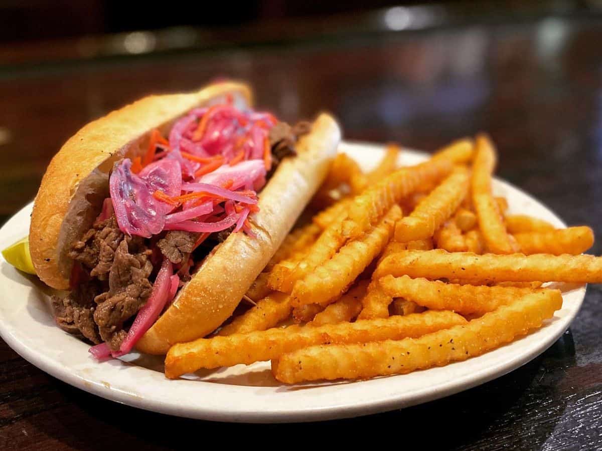 A Korean bulgogi sandwich topped with Asian slaw and a side of seasoned fries at Willie's Sports Pub.