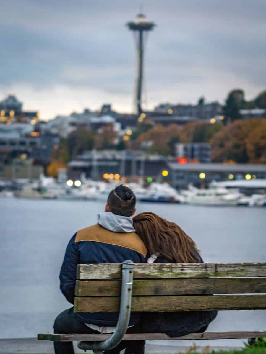 A couple enjoying the view of the Seattle Space Needle from Gas Works Park at sunset.