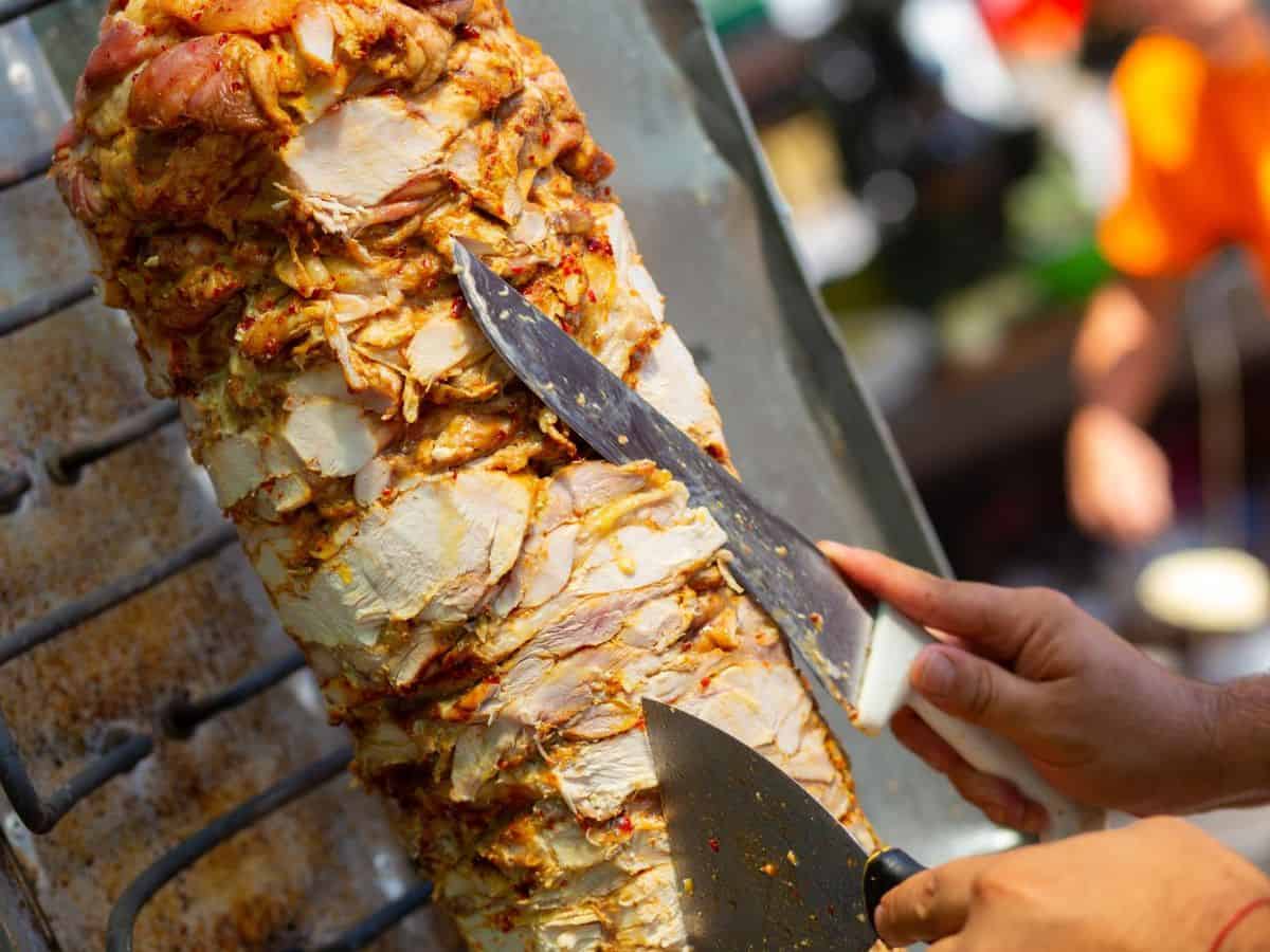 A person expertly cuts meat for a kebab.