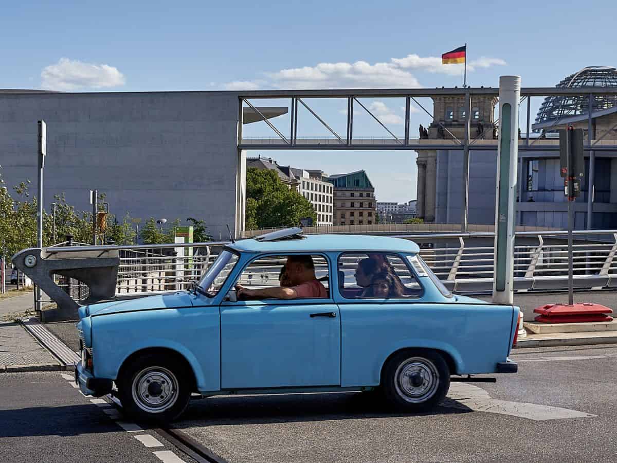A small blue Trabant car driving down a street in Berlin.