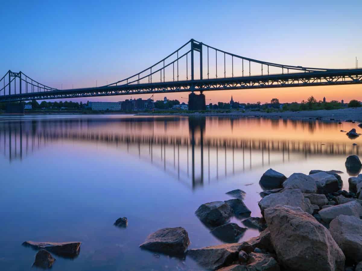 A bridge over the Rhine River is reflected in the water at dusk.