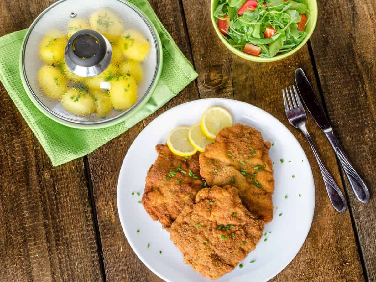 A delicious German schnitzel, served with golden potatoes and a fresh salad, on a plate.