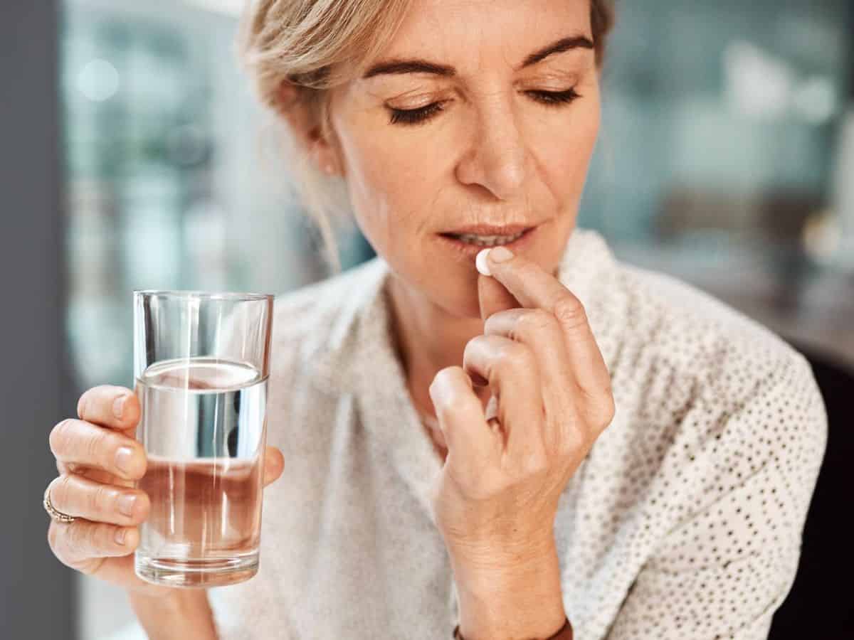 A woman is taking an aspirin with a glass of water.