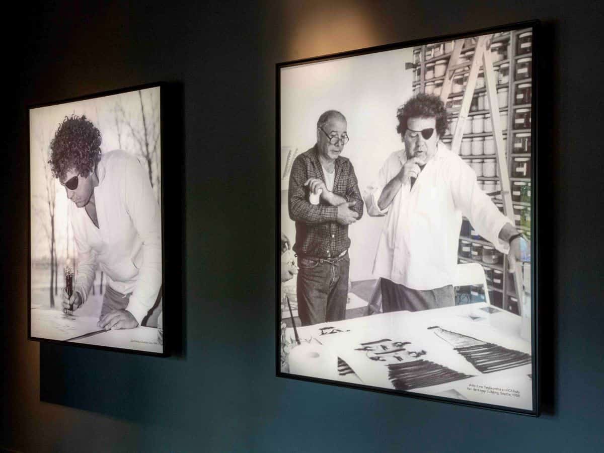 Two black and white photographs of Dale Chihuly hanging on a wall at his museum in Seattle.