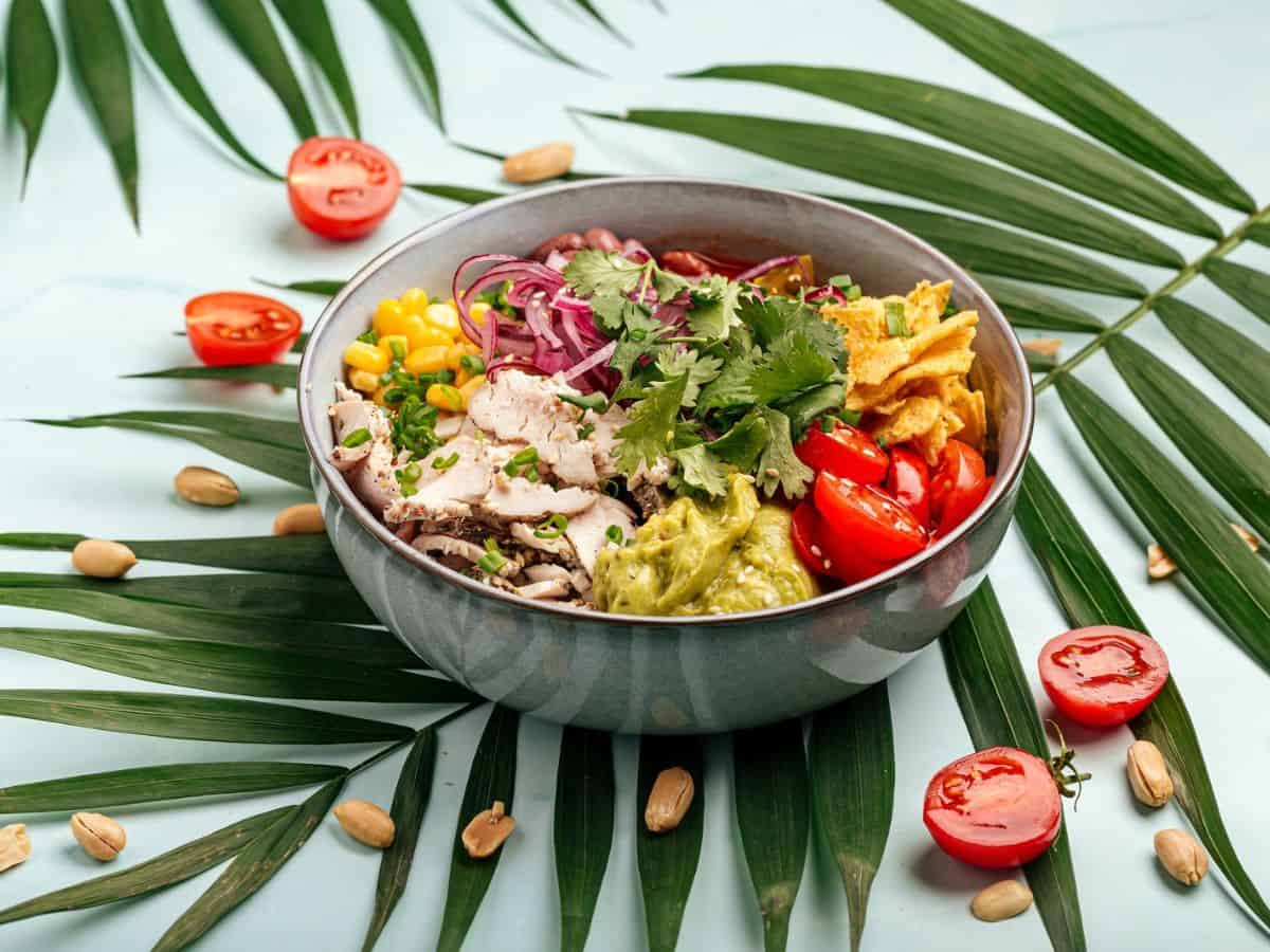 A Hawaiian chicken poke bowl on a blue background with palm leaves.