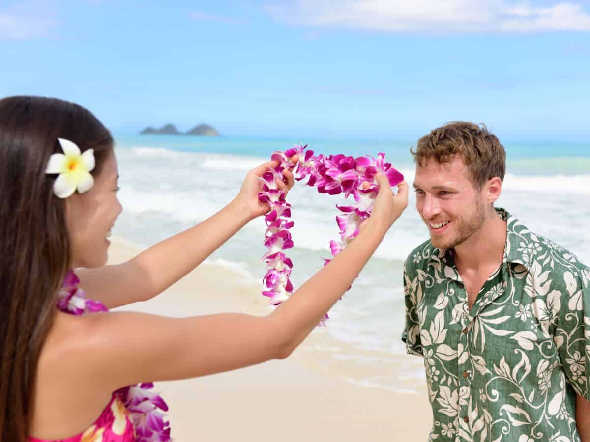 A woman placing a flower lei around a luau guest's neck.