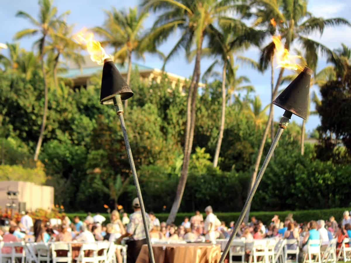 Guests sitting at white tables beneath palm trees at a Hawaiian luau.
