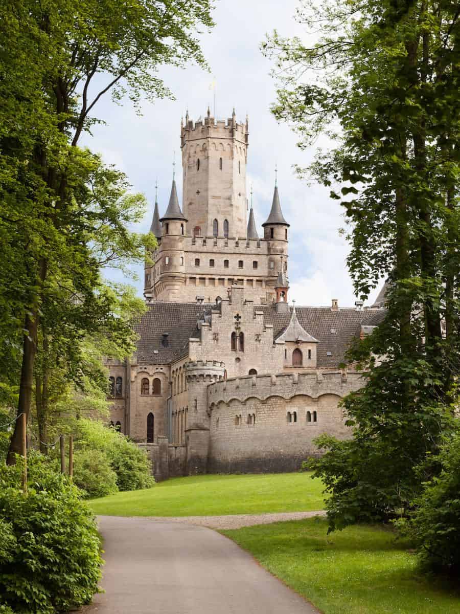 A German castle nestled amidst a lush forest and a winding path.