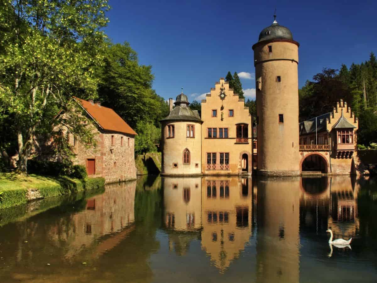A German castle in the middle of a lake with a swan in the water.