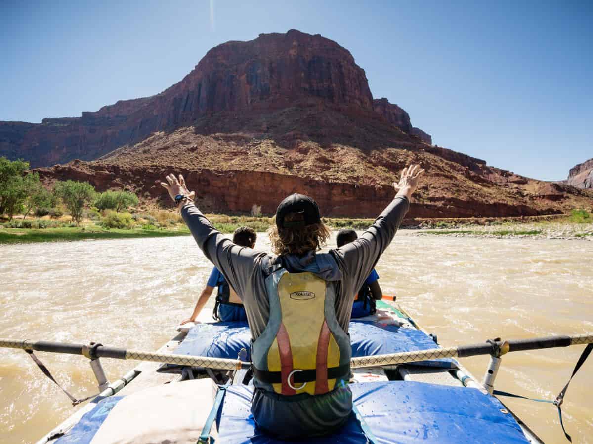 A group of people in a blue raft on the Colorado River surrounded by beautiful Utah scenery.