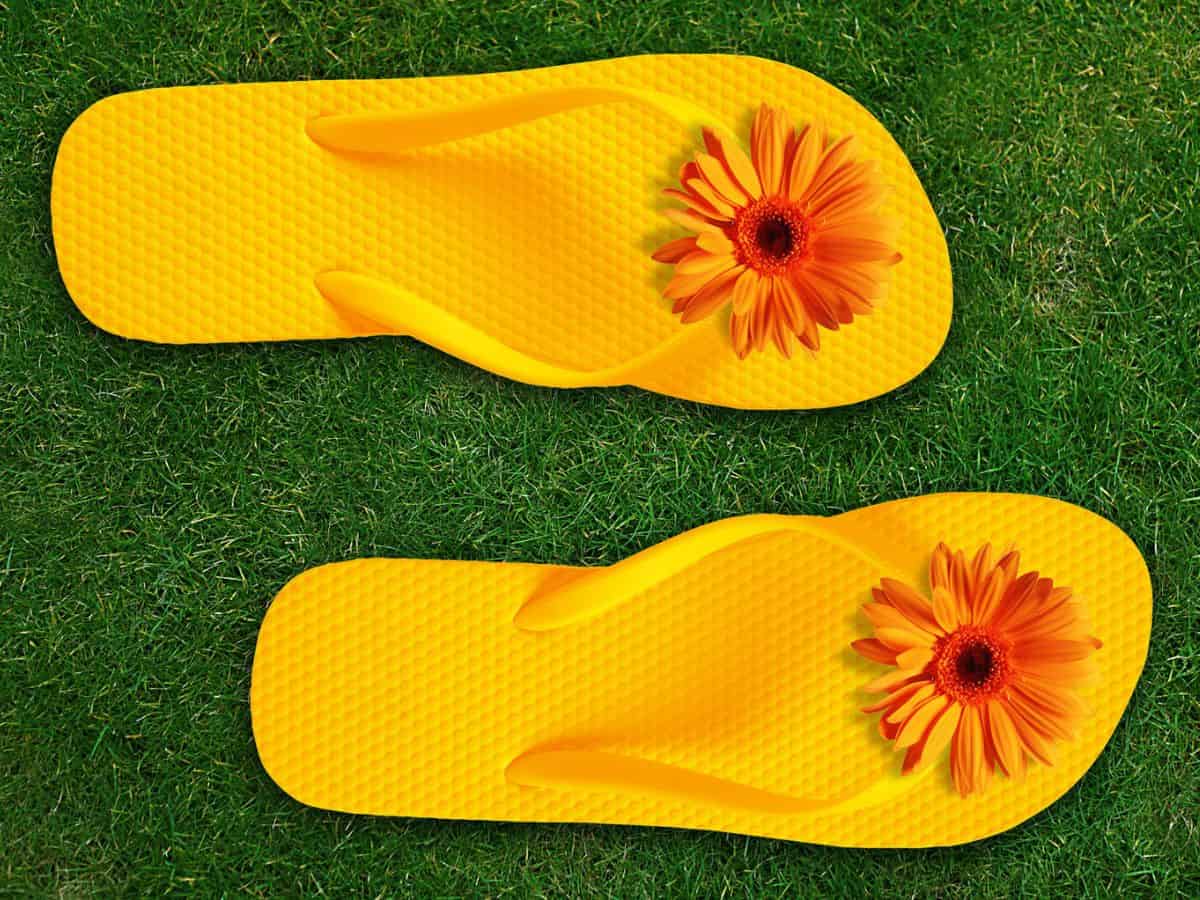 Two yellow flip flops with a flower on the grass, perfect for a luau.