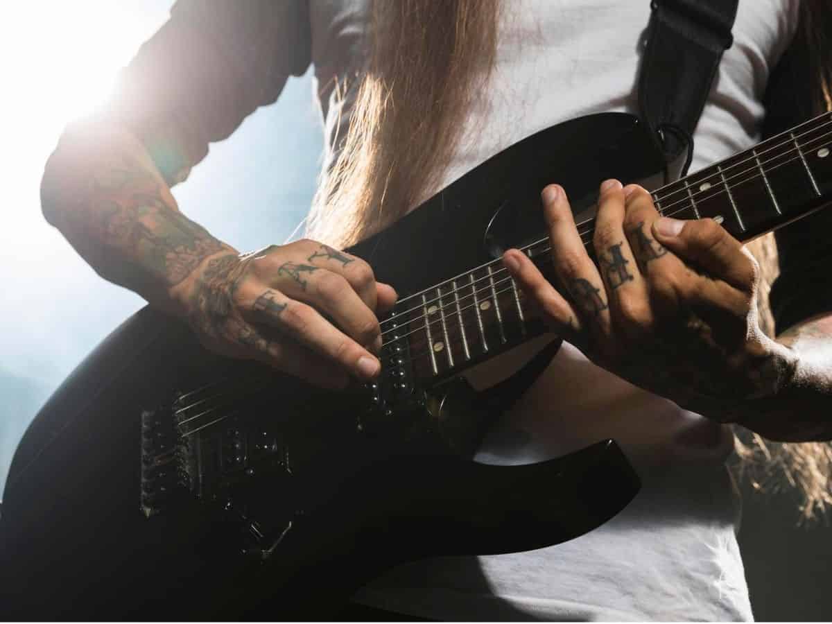 A man with long hair and tattoos enthusiastically playing an electric guitar.