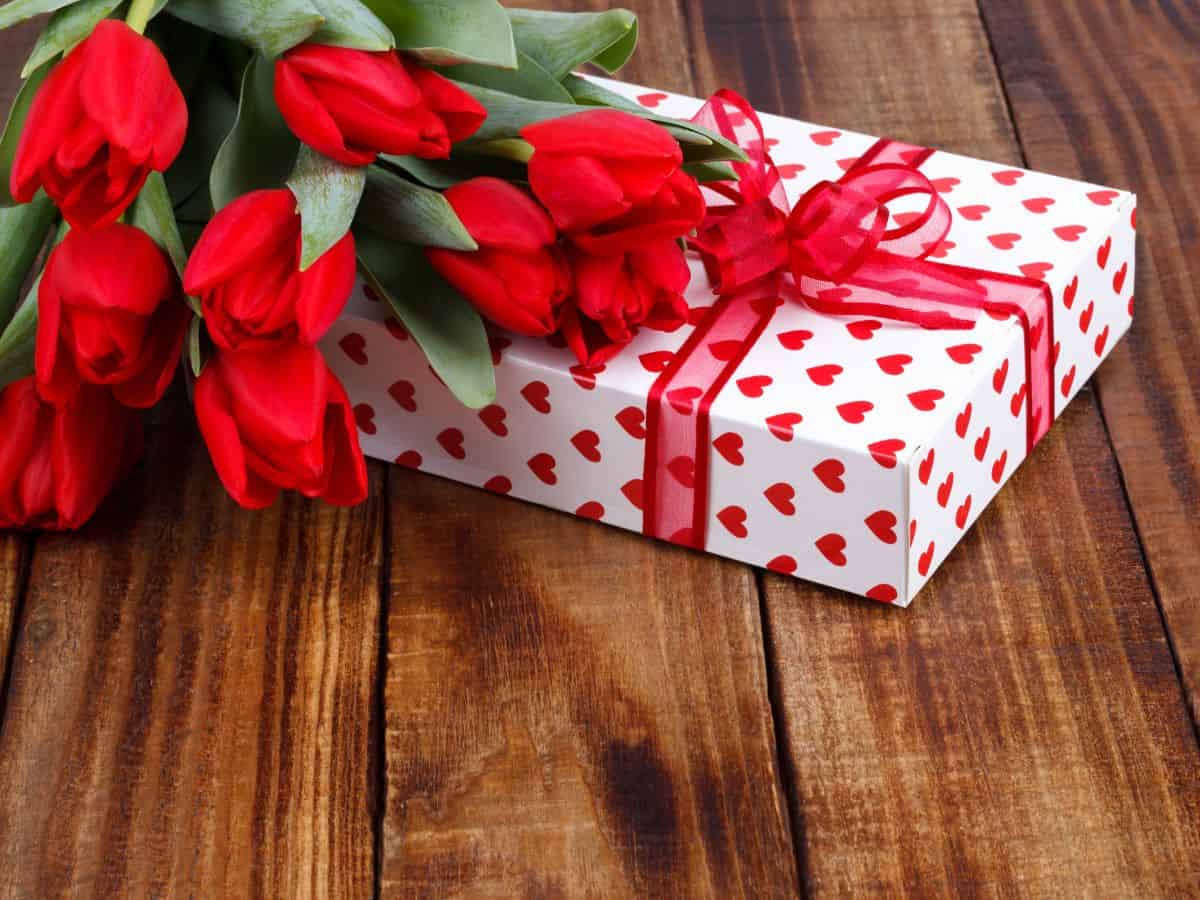A vibrant bouquet of red tulips is elegantly displayed alongside a charming gift box on a rustic wooden table.