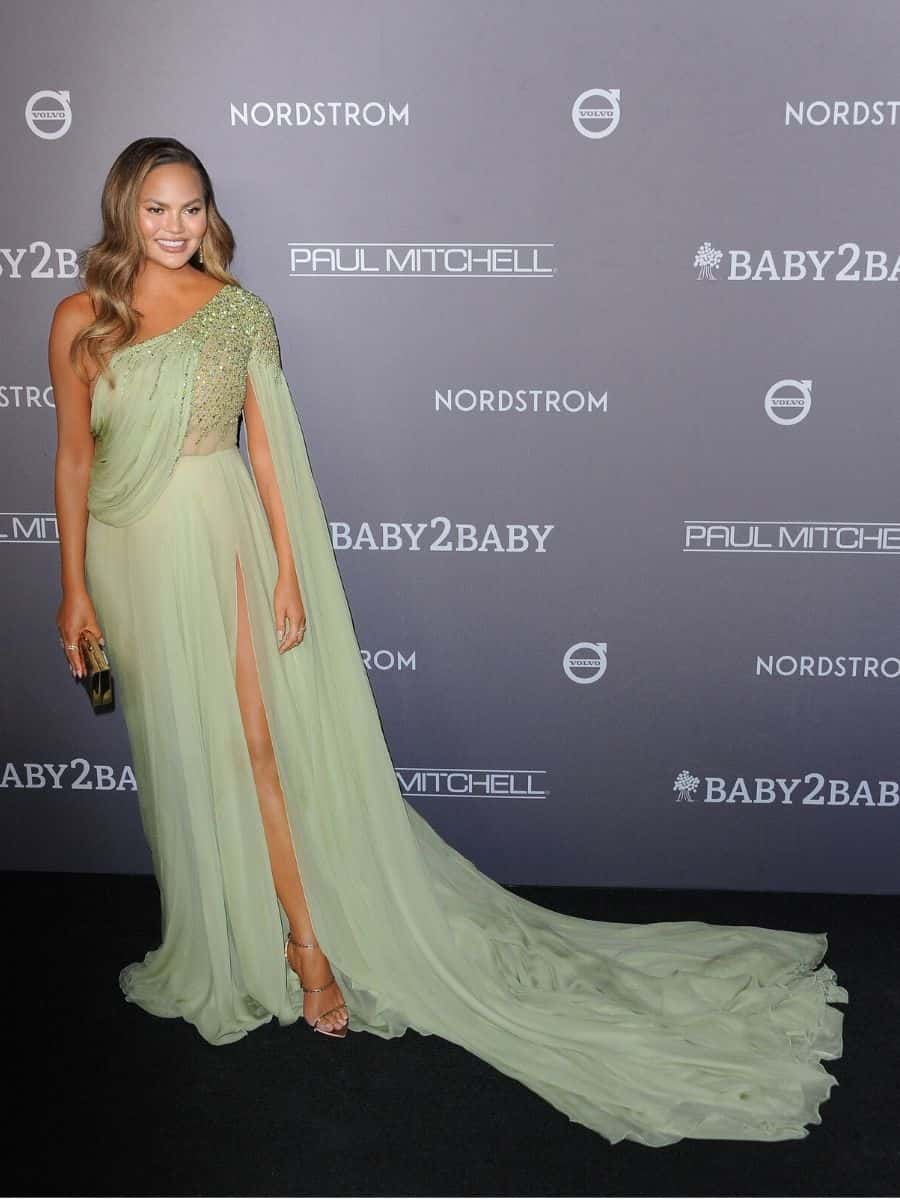 Chrissy Teigen poses in a green gown on the black carpet at an event.