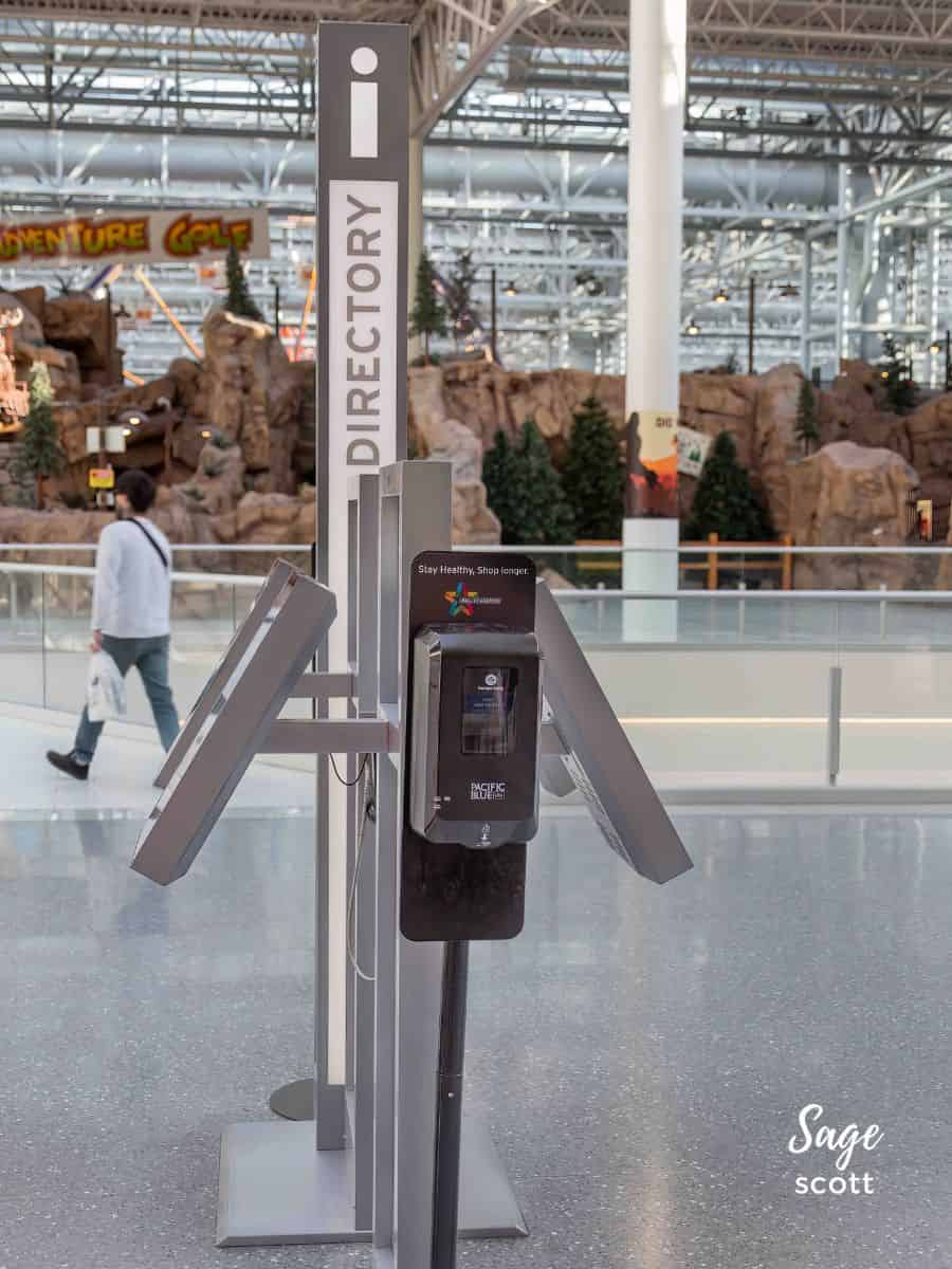 A person is walking past a kiosk in an airport, possibly noticing interesting facts about Mall of America.