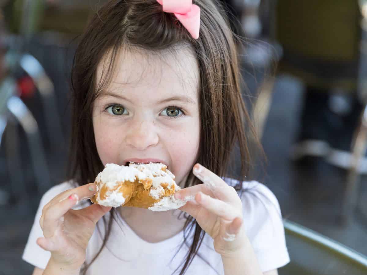 A little girl eating a beignet.