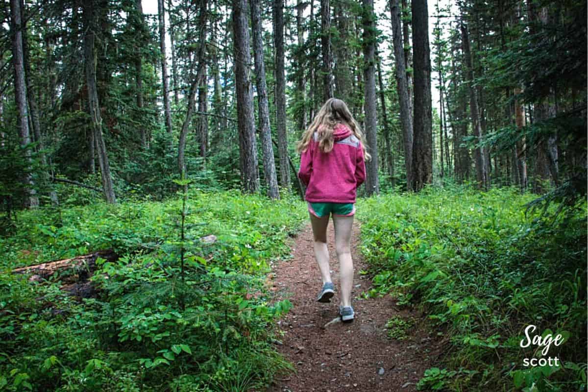 A girl is running down a scenic trail in the woods of Montana.