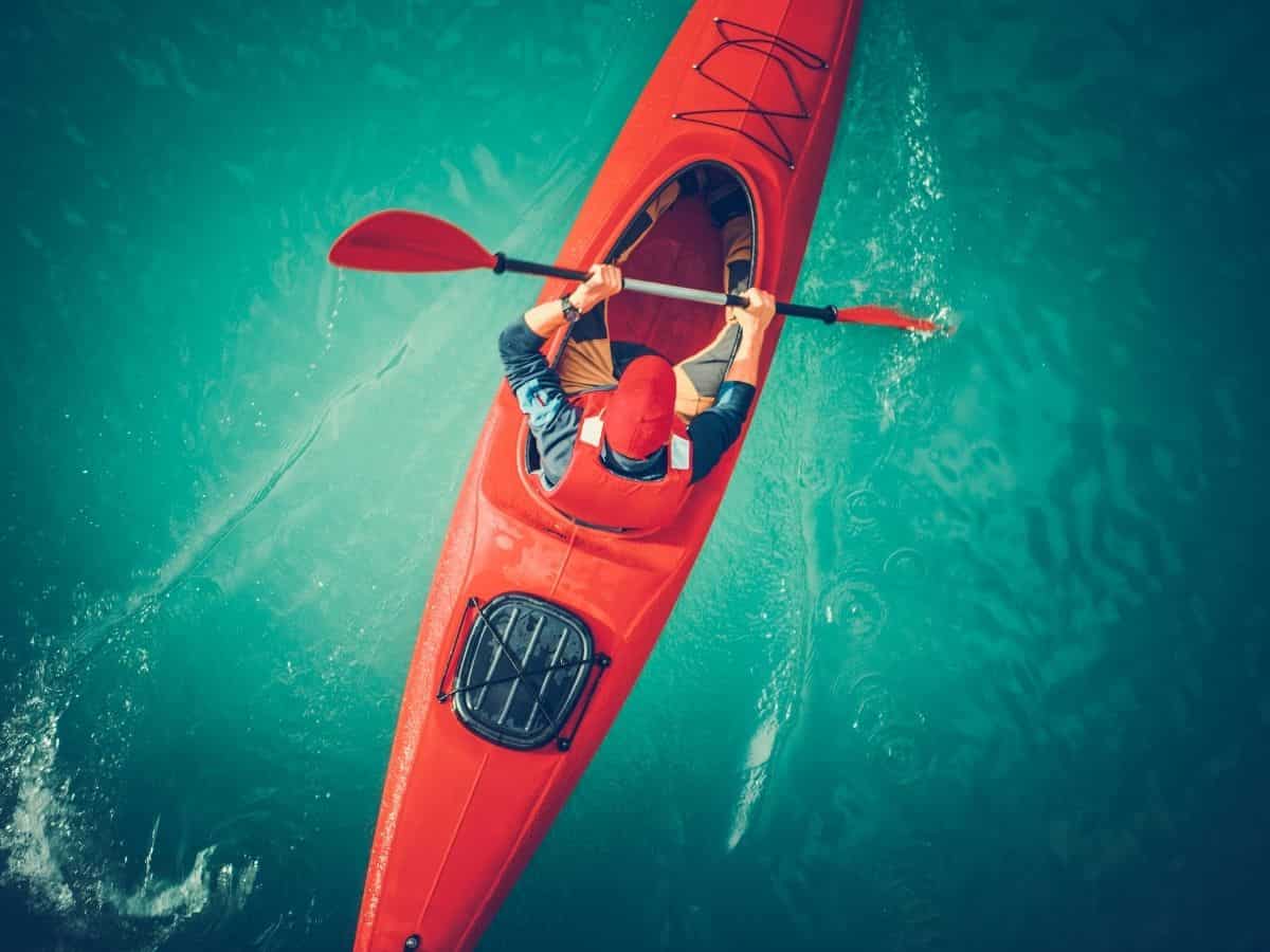 A man is paddling a red kayak in the water.