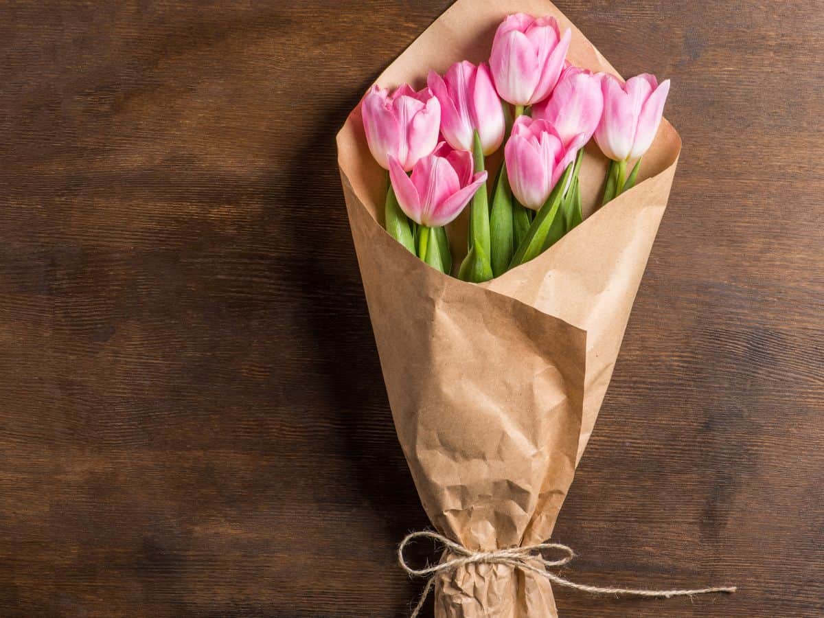 Pink tulips in a paper bag on a wooden table representing the meaning of tulip colors.