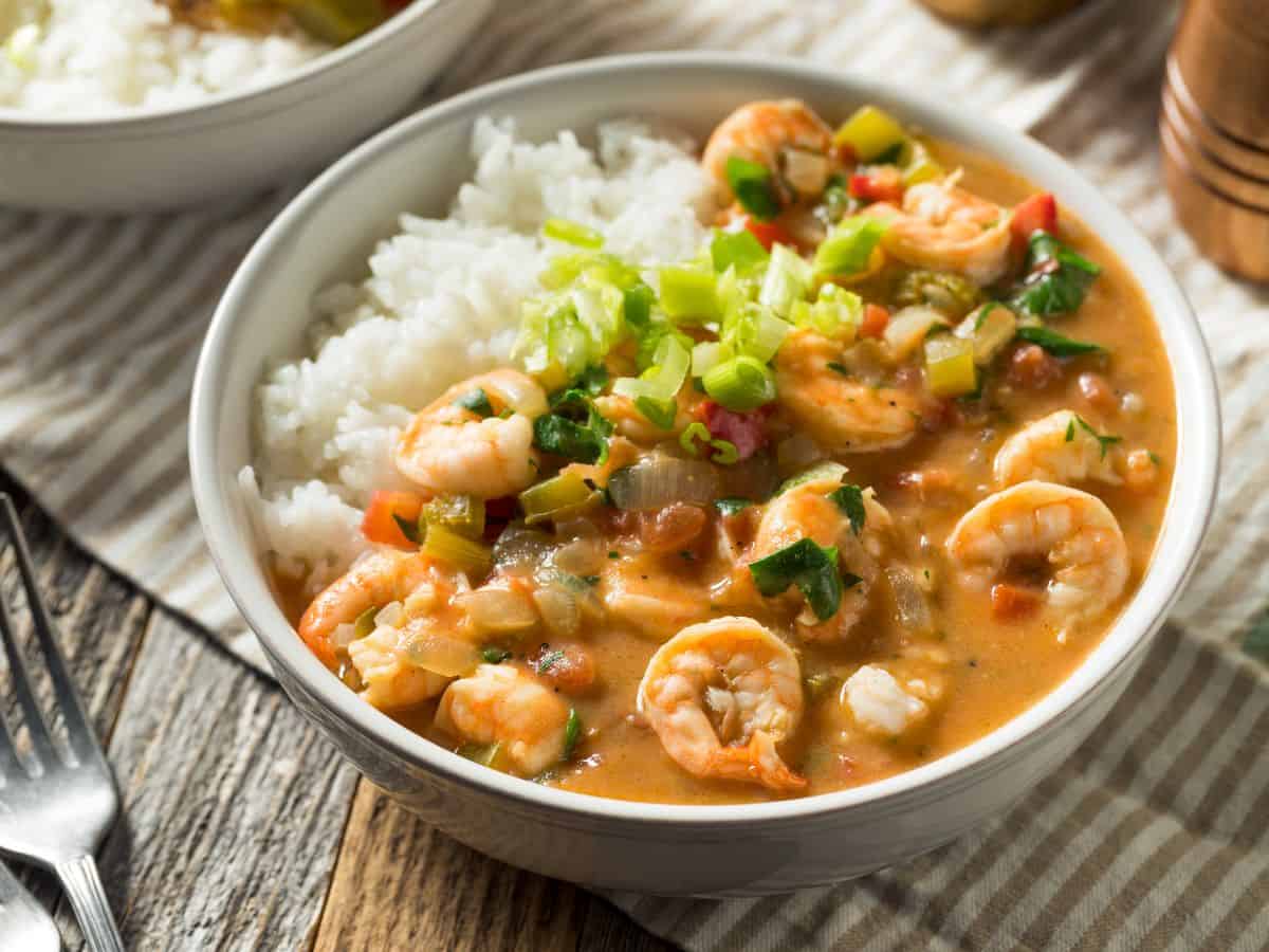 A bowl of shrimp etouffee with rice on a wooden table.
