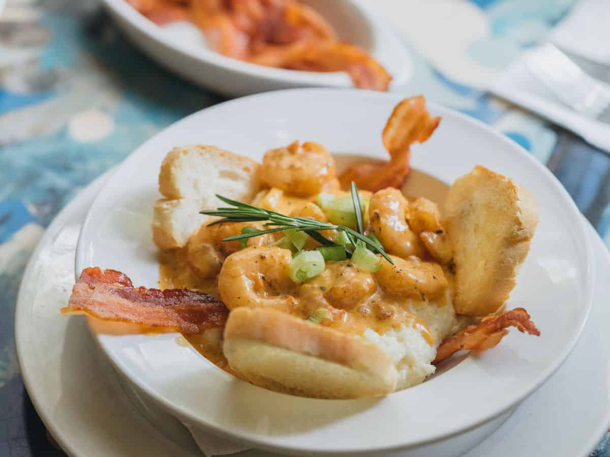 A bowl of shrimp and grits with bacon and bread.